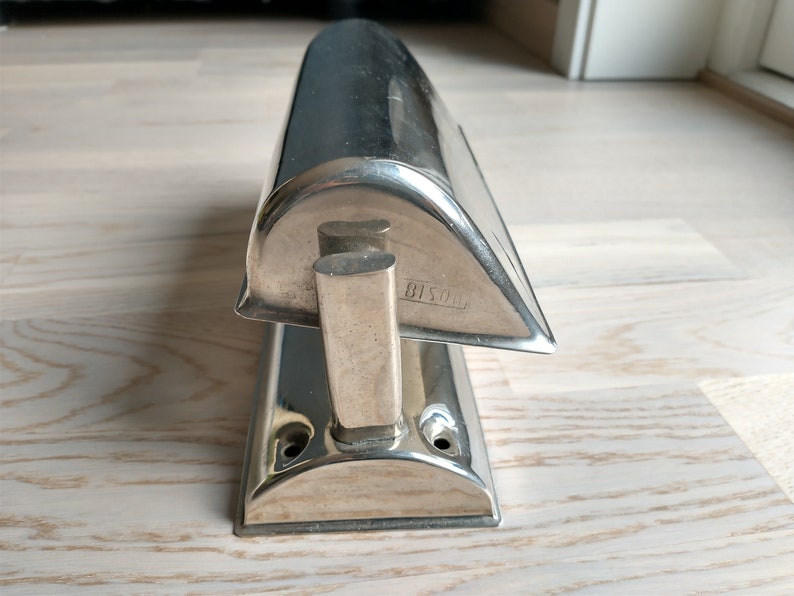 May include: A silver-toned metal doorstop shaped like a boat with a rounded top and a flat base. The doorstop has a small handle on the side and the text "8150" is engraved on the side.