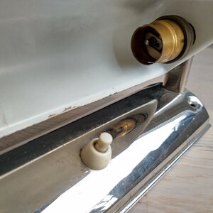 May include: A white and chrome wall light fixture with a brass light bulb socket and a white toggle switch.