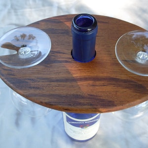 May include: Wooden wine bottle holder with two glass holders. The bottle holder is brown with a wood grain pattern. The glass holders are clear glass.