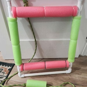 May include: A white PVC frame with pink and green foam pool noodles. The frame has a mesh center and is connected with rope. The frame is designed for aquatic exercise and fitness.