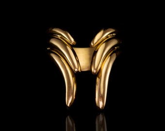 May include: A gold ring with a unique design featuring two curved, overlapping bands that form a V-shape.