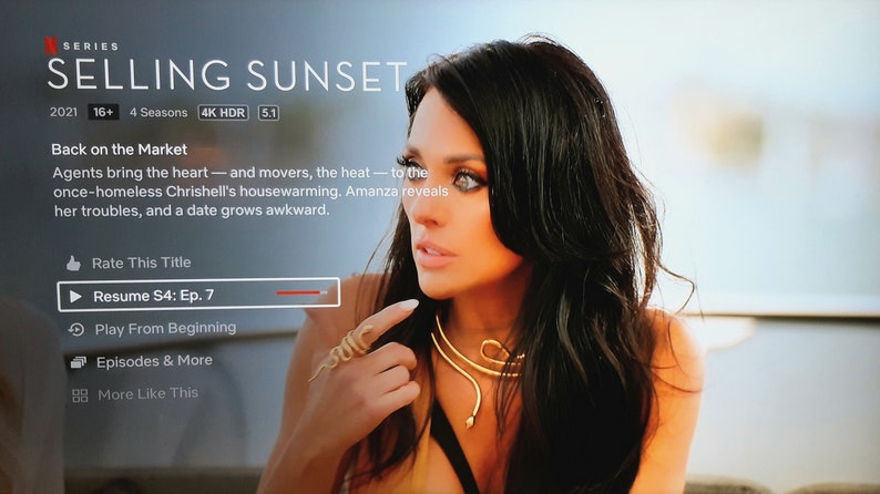 May include: A screenshot of the Netflix show "Selling Sunset" with a woman in the foreground. The text "Back on the Market" is displayed above the woman. The text "Agents bring the heart - and movers, the heat - to the once-homeless Chrishell's housewarming. Amanza reveals her troubles, and a date grows awkward." is displayed below the woman. The text "Resume S4: Ep. 7" is displayed in a red bar at the bottom of the screen.