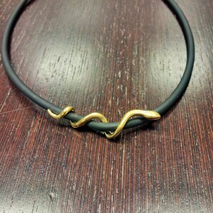 May include: A black rubber choker necklace with a gold snake charm.
