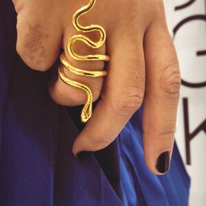 May include: A gold snake ring with a coiled design. The ring is worn on a finger and the snake's head is pointing upwards.