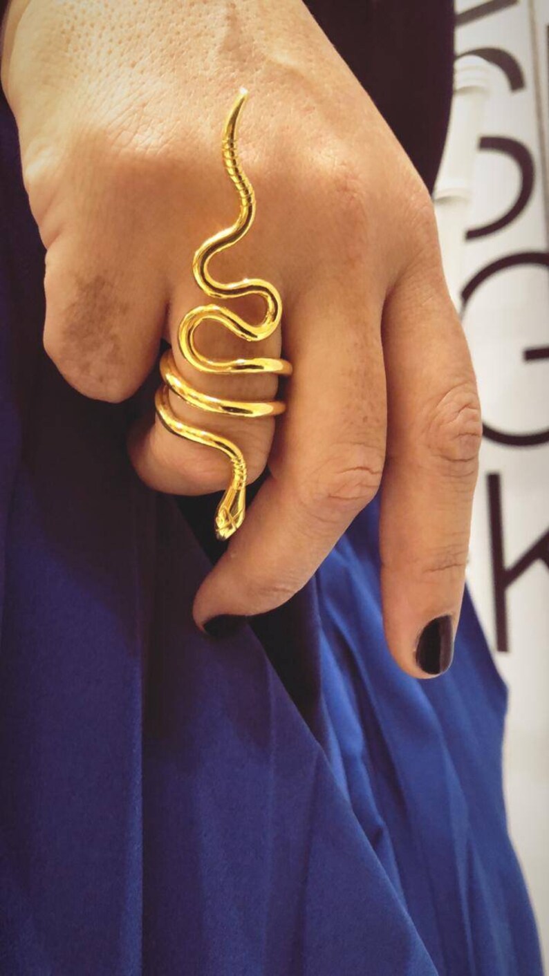 May include: A gold snake ring with a coiled design. The ring is worn on a finger and the snake's head is pointing upwards.