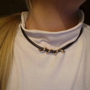 May include: A black choker necklace with a gold, twisted, snake-like pendant.