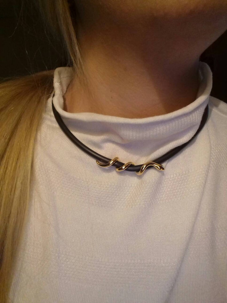 May include: A black choker necklace with a gold, twisted, snake-like pendant.
