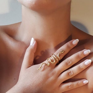 May include: A gold snake ring with a coiled design. The ring is worn on the index finger of a hand.