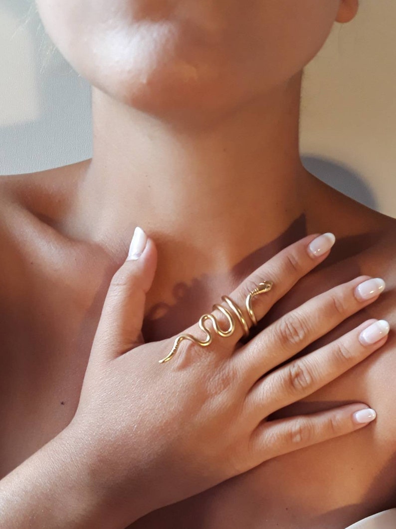 May include: A gold snake ring with a coiled design. The ring is worn on the index finger of a hand.