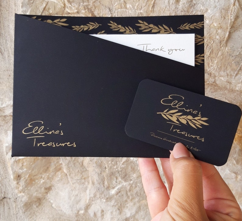 May include: Black envelope with gold leaf design and the text "Ellina's Treasures" on the front. A white card with the text "Thank you" is inside the envelope. A black gift card with gold leaf design and the text "Ellina's Treasures" is on top of the envelope.
