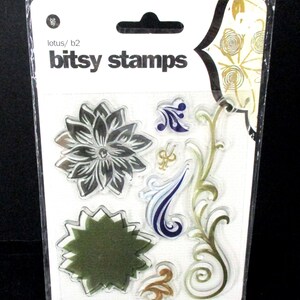 May include: A clear plastic package containing a set of eight clear rubber stamps with floral and vine designs. The stamps are in shades of gold, green, blue, and black. The package is labeled "bitsy stamps" and "lotus/b2".