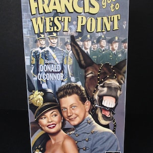 Puede incluir: Una carátula de casete de vídeo VHS con un burro de dibujos animados y una pareja frente a un grupo de hombres militares. El título de la película es "FRANCIS goes to WEST POINT" y la estrella es "DONALD O'CONNOR".