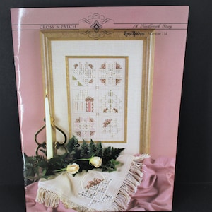 May include: A cross stitch pattern booklet titled "Cross 'n Patch" with a needlework story by Annie Bishop, number 114. The cover features a framed cross stitch design with a floral motif and a white linen doily with a cross stitch design.