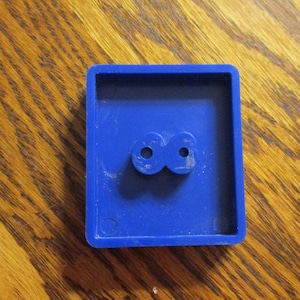 May include: A blue plastic square with two round holes in the center.