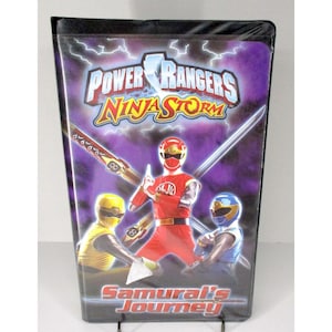 Op de afbeelding: Een verzegelde dvd-hoes voor Power Rangers Ninja Storm. De cover toont drie Power Rangers in rode, gele en blauwe uniformen, met het titellogo en de woorden "Samurai's Journey" onderaan. De achtergrond is een paars en blauw bliksemontwerp.