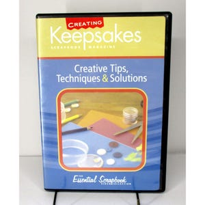 May include: DVD case with a blue background and a red and yellow title that reads "Creating Keepsakes Scrapbook Magazine". The subtitle reads "Creative Tips, Techniques & Solutions". The image shows a close-up of a craft project with various craft supplies, including pencils, scissors, and buttons.