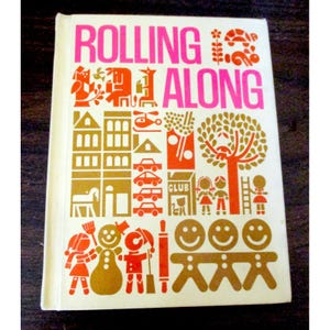 May include: A vintage book cover with the title "ROLLING ALONG" in pink. The cover features orange and gold illustrations of buildings, cars, people, and other whimsical images. The book has a cream-colored background.