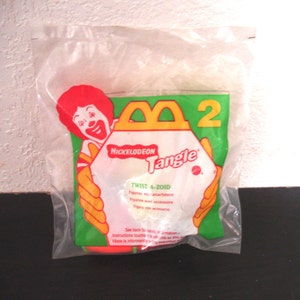 May include: A clear plastic bag with a red and yellow McDonald's Happy Meal toy inside. The toy is a Nickelodeon Tangle Twist-A-Zoid figure. The bag has a green and yellow background with the McDonald's logo and the words "Nickelodeon Tangle" printed on it.