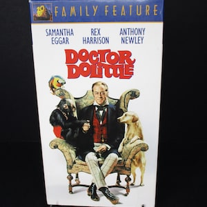 Puede incluir: Una caja de cinta VHS para la película "Doctor Dolittle" con Rex Harrison, Samantha Eggar y Anthony Newley. La portada muestra a Rex Harrison sentado en una silla con un mono y un perro.