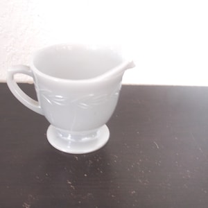 Könnte beinhalten: Ein weißer Milchglas-Sahnegießer mit einem Fuß und einem Blattdesign.