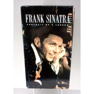 Puede incluir: Una caja con un retrato de Frank Sinatra. Las palabras "FRANK SINATRA" están en letras mayúsculas blancas en la parte superior, con "PORTRAIT OF A LEGEND" debajo. La imagen es un primer plano de Sinatra sonriendo.