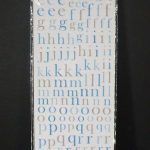 May include: A sheet of blue and gray rub-on letters and numbers for journaling. The sheet includes the alphabet, numbers 1-9, and symbols like ampersand and exclamation point. The sheet is packaged in a clear plastic bag with a header that reads "journaling alphabet 238 pieces".