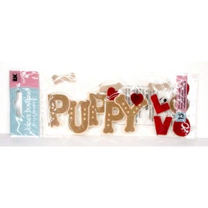 Może przedstawiać: Opakowanie ozdób rzemieślniczych ze słowem "PUPPY" w brązowych literach z białymi kropkami oraz słowem "LOVE" w czerwonych literach. Zawiera czerwone kształty serc i kształt kości. Opakowanie zawiera również etykietę z tekstem "dolce's boutique".