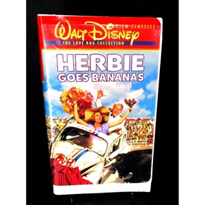 May include: A VHS tape for the Disney film "Herbie Goes Bananas" from The Love Bug Collection. The cover features a colorful image of a white Volkswagen Beetle in a bullring, with the title in large, bold letters.