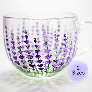 May include: A clear glass teacup with a handle, hand-painted with purple lavender sprigs. The lavender design is painted on the outside of the cup, with green stems at the base. The cup is available in 2 sizes.