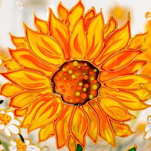 Op de afbeelding: Een handbeschilderd glazen oppervlak met een grote, levendige zonnebloem met felgele en oranje bloemblaadjes. Het midden van de bloem is donkerbruin met verspreide gele en oranje stippen. Kleinere witte madeliefjes zijn onderaan zichtbaar.