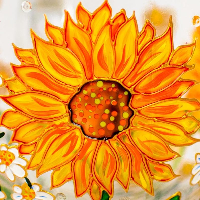 Op de afbeelding: Een handbeschilderd glazen oppervlak met een grote, levendige zonnebloem met felgele en oranje bloemblaadjes. Het midden van de bloem is donkerbruin met verspreide gele en oranje stippen. Kleinere witte madeliefjes zijn onderaan zichtbaar.