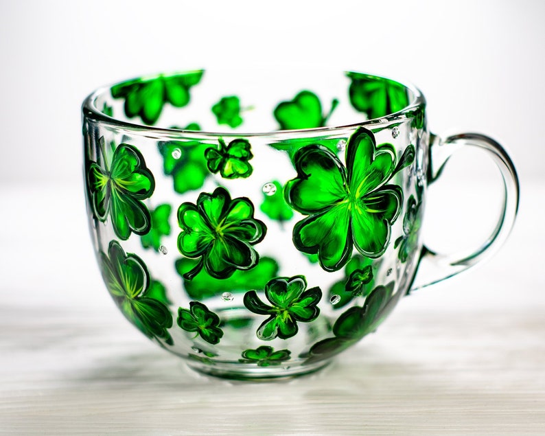 Hand painted shamrock mug with green four leaf clovers on clear glass.