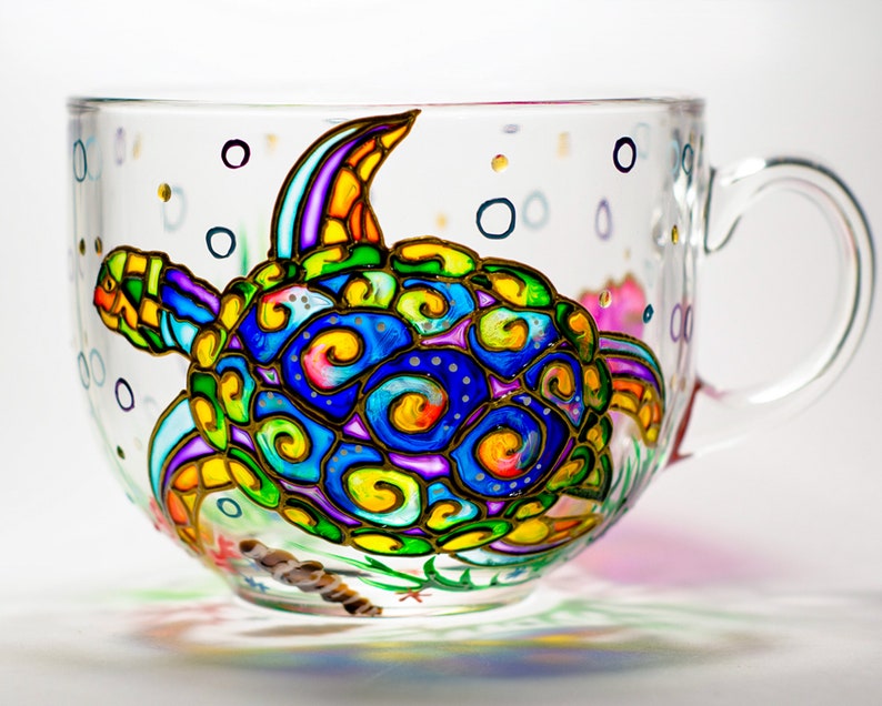 May include: A glass mug with a hand-painted design of a colorful sea turtle with swirls and bubbles. The turtle is painted in shades of blue, green, yellow, orange, and purple.