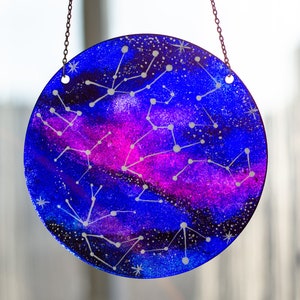 May include: A round glass bauble with a blue and purple galaxy design and white constellations painted on it. The bauble is hanging from a silver chain.