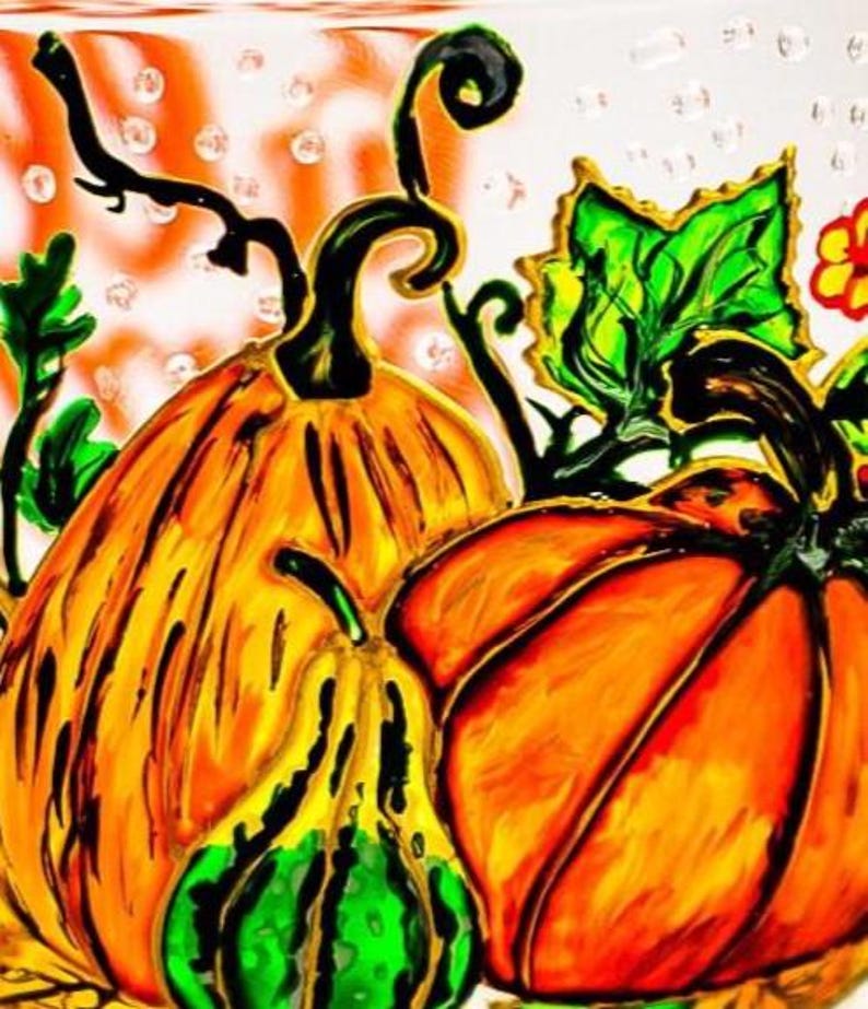 May include: A glass surface featuring a hand-painted illustration of two large orange pumpkins and a smaller green and yellow gourd. The design includes black outlines, vibrant green leaves, and curly vines against a translucent background.