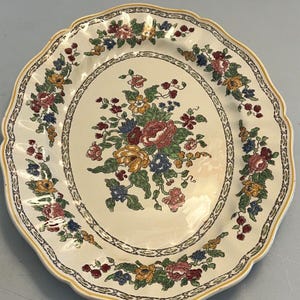 Könnte beinhalten: Cremefarbene Servierplatte mit gewelltem Rand und floralem Design. Die Mitte zeigt einen Strauß aus roten, gelben, blauen und rosa Blumen. Ein dekorativer Blumenrand und ein gelber Rand vervollständigen das Design. Ein Stück im Vintage-Stil.