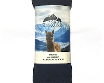 May include: A pair of navy blue alpaca socks. The packaging features the text "ALASKAN ALPACAS" above an image of an alpaca with a mountain backdrop. The text "MEN'S OUTDOOR ALPACA SOCKS" is also visible.