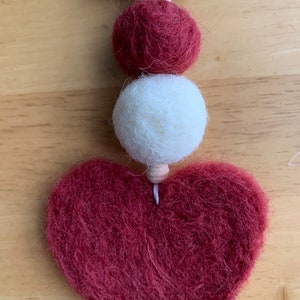 May include: A burgundy felt heart ornament with two white and burgundy felt balls and a wooden bead hanging from a wooden clothespin.