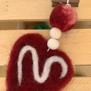May include: A burgundy felt heart with a white felt swirl design, hanging from a string with wooden beads and a burgundy felt ball.