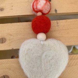 May include: A white felt heart ornament with a red and white felt ball and a red felt ball hanging from it.