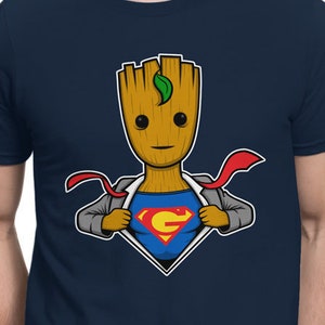 May include: A navy blue t-shirt with a cartoon image of a superhero Groot, a character from the Guardians of the Galaxy, wearing a Superman costume. The image shows Groot ripping open his shirt to reveal the Superman costume underneath.