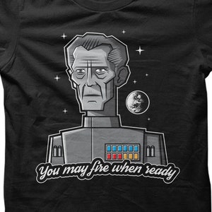 May include: A black t-shirt with a cartoon illustration of a man in a space uniform. The text "You may fire when ready" is printed below the illustration.