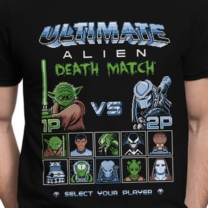 May include: Black t-shirt with a pixelated graphic of a video game screen. The text "Ultimate Alien Death Match" is at the top of the screen. The characters Yoda and Predator are in the center of the screen. The text "Select Your Player" is at the bottom of the screen.