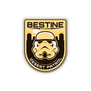 May include: A yellow and black patch featuring a Stormtrooper helmet. The patch reads "BESTINE TATOOINE DESERT PATROL IMPERIAL STORMTROOPER CORPS" in a stylized font. The background depicts a desert landscape with a setting sun.