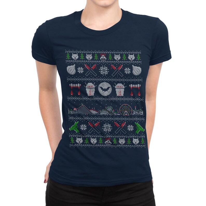 Puede incluir: Una camiseta azul marino con un dise&ntilde;o de su&eacute;ter navide&ntilde;o blanco, rojo y verde que presenta un murci&eacute;lago, ajo, cuchillos y una monta&ntilde;a rusa. El dise&ntilde;o recuerda a una pel&iacute;cula de terror.