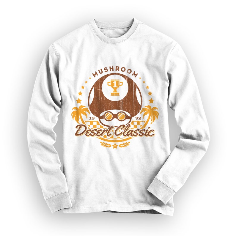May include: White long-sleeve shirt with a distressed graphic. The graphic features a brown mushroom with a trophy, sunglasses, palm trees, and the text "Mushroom Desert Classic 1992". The design is in shades of brown and orange.
