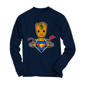 May include: Navy blue long-sleeve t-shirt featuring a cartoon image of a superhero Groot, a tree-like humanoid character from the Guardians of the Galaxy franchise, wearing a Superman costume. The image shows Groot ripping open his shirt to reveal the Superman symbol.