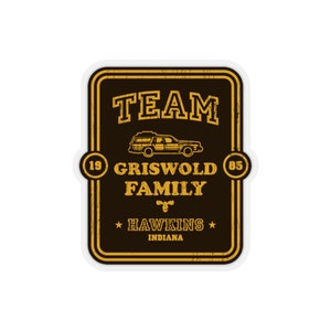 Könnte beinhalten: Ein gelber und brauner Aufkleber im Vintage-Stil mit dem Text "TEAM GRISWOLD FAMILY" und einer kleinen Autoillustration. Der Aufkleber enthält auch den Text "19 85" und "HAWKINS INDIANA".