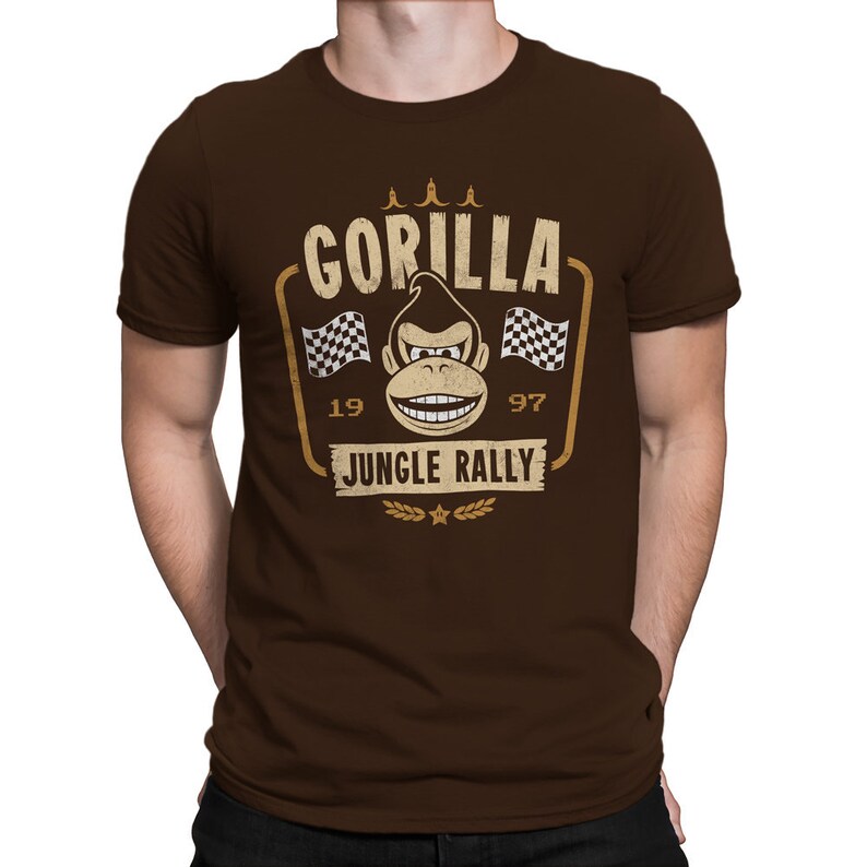 May include: A brown t-shirt with a vintage-style graphic of a gorilla wearing a racing helmet and driving a race car. The graphic says "Gorilla Jungle Rally" with the numbers "19" and "97" on either side.