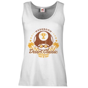 May include: White tank top with a distressed graphic featuring a brown mushroom with sunglasses, a trophy, palm trees, and the text "Mushroom Desert Classic 1992". The design is in shades of brown and gold.